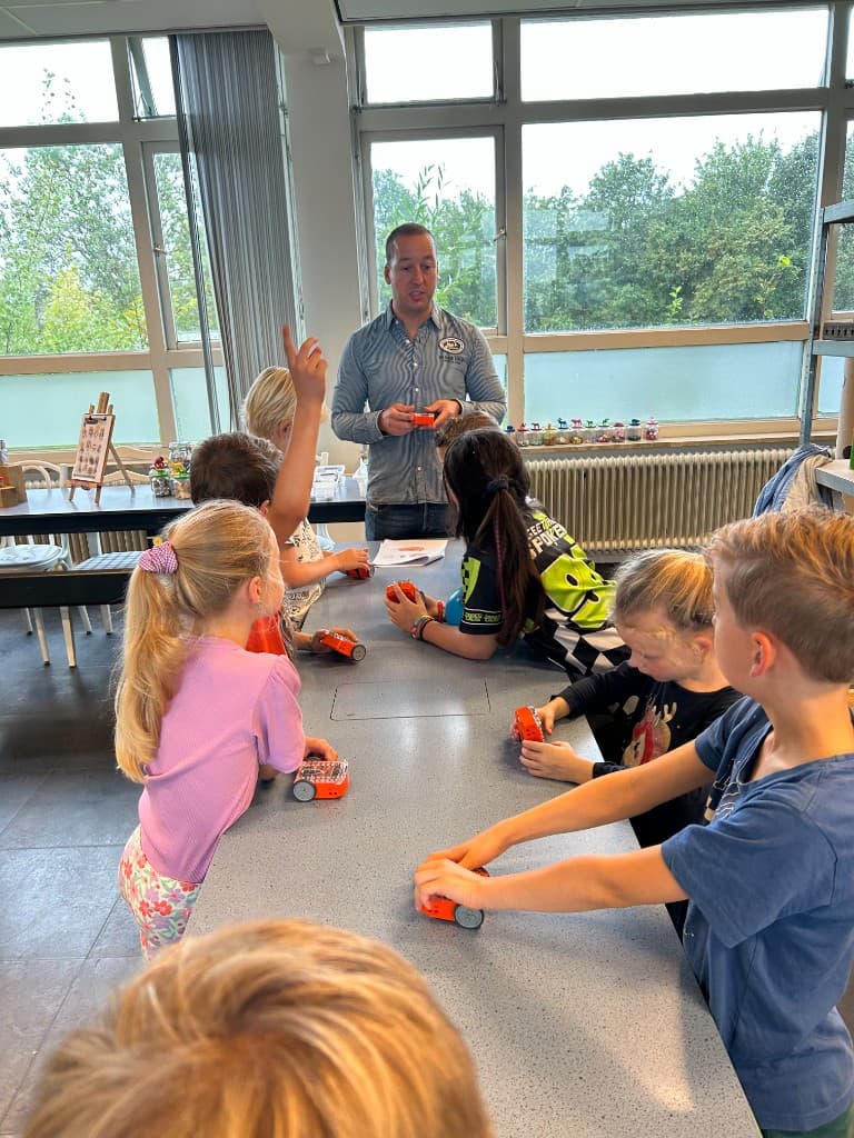 Kinderen rond een tafel met Edison-robots terwijl een begeleider uitleg geeft